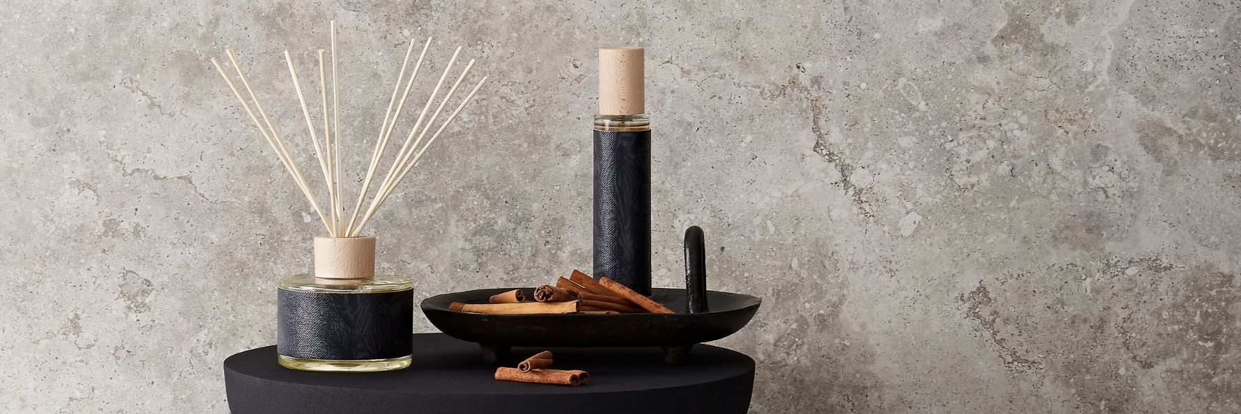 Diffuseur à bâtonnets et bougie parfumée Decoragloba devant un mur de pierre
